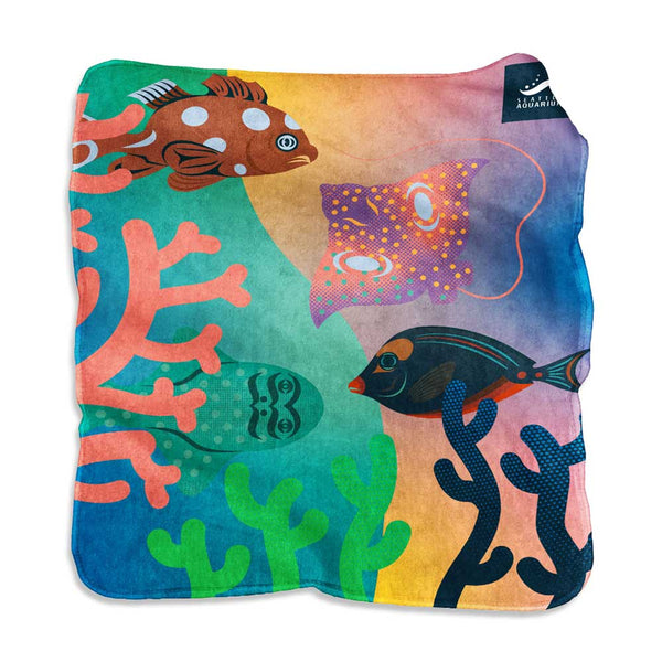 The Seattle Aquarium Pettibon Blanket showcases a vibrant underwater scene with coral, a grouper fish, a tang fish, a spotted moray eel, and two patterned stingrays inspired by the Salish Sea.