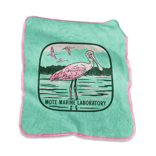 The Mote Marine Laboratory Raschel Blanket is a green cloth blanket with pink trim, showcasing an illustration of a spoonbill bird standing in water, surrounded by flying birds and trees in the background. The text “MOTE MARINE LABORATORY” appears below the image, reflecting a commitment to marine conservation.
