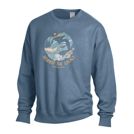 The Seattle Aquarium Respect the Locals Sweatshirt features a blue crewneck design with an illustration of an orca leaping over waves, framed by trees and mountains. Below the image is the text “RESPECT THE LOCALS” along with “Seattle, Washington.” This marine life sweatshirt makes a perfect ocean conservation gift for anyone who loves the Pacific Northwest.