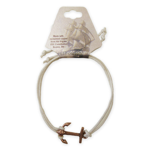 The Adjustable Cord Bracelet features a small copper anchor charm made from reclaimed USS Constitution copper, on a white cord, displayed on a card with a ship illustration and details about its Boston, MA origin.