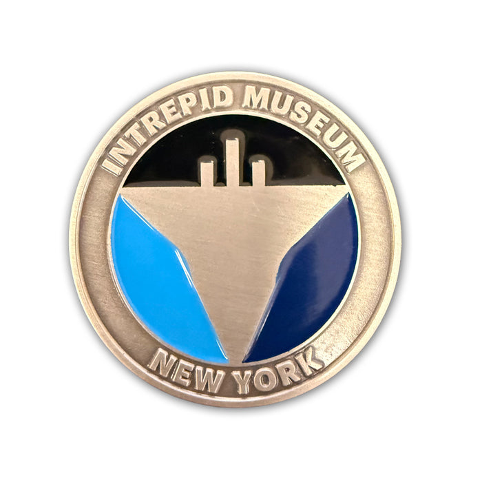 Introducing the Intrepid Museum Challenge Coin—a round pin inspired by traditional challenge coins, showcasing a stylized aircraft carrier silhouette with silver, black, light blue, and navy blue segments, and featuring the “Intrepid Museum New York” text.