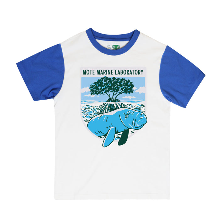 The Mote Marine Laboratory Manatee Ringer Youth T-Shirt is a kids’ t-shirt made from soft organic cotton, featuring blue sleeves and a graphic of a manatee swimming beside a mangrove tree and water, with the text “Mote Marine Laboratory” above the image.