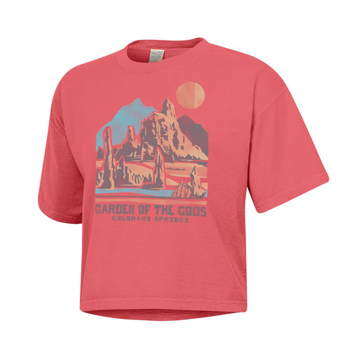The Garden of the Gods Iconic Rocks Women’s Crop T-Shirt is a coral crop top made with eco-friendly materials, featuring a graphic of rock formations, a sun, and mountains. The text below reads “Garden of the Gods Colorado Springs.”.