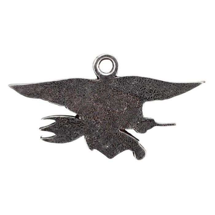 The Navy SEAL Museum Pewter Ornament is a handcrafted, dark metal pendant depicting an eagle in flight clutching a trident and a flintlock-style pistol, with a small loop at the top for hanging—this striking ornament is inspired by artifacts displayed at the Navy SEAL Museum.