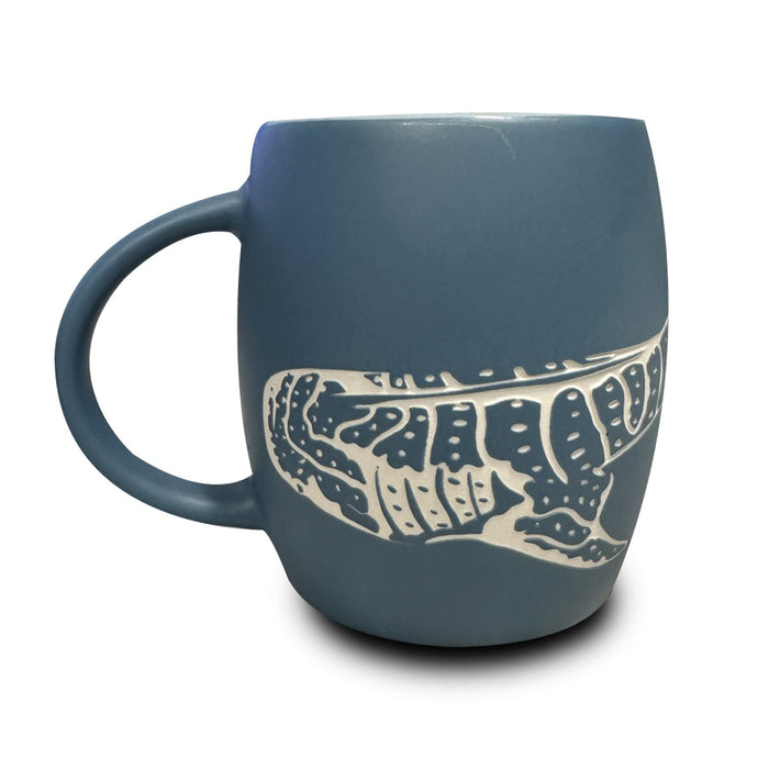 The Georgia Aquarium Whale Shark Etched Mug is a blue ceramic mug showcasing a white and dark blue illustration of a whale shark wrapping around its side, reminiscent of the graceful giants at the Georgia Aquarium, displayed on a white background.
