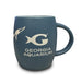 The Georgia Aquarium Whale Shark Etched Mug is a blue ceramic mug featuring an etched shark silhouette and the “G Georgia Aquarium” logo in white, with a large curved handle on the right.