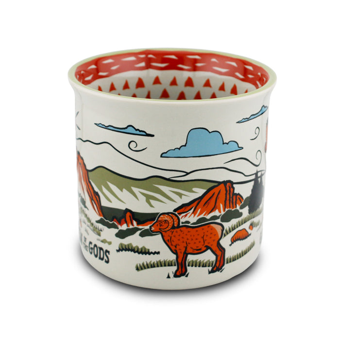 Garden of the Gods Feeling Folksy Mug – a ceramic cup featuring colorful illustrations of a ram, mountains, clouds, and red rock formations inspired by Colorado Springs’ iconic Garden of the Gods. The interior showcases a vibrant red and white triangular pattern.