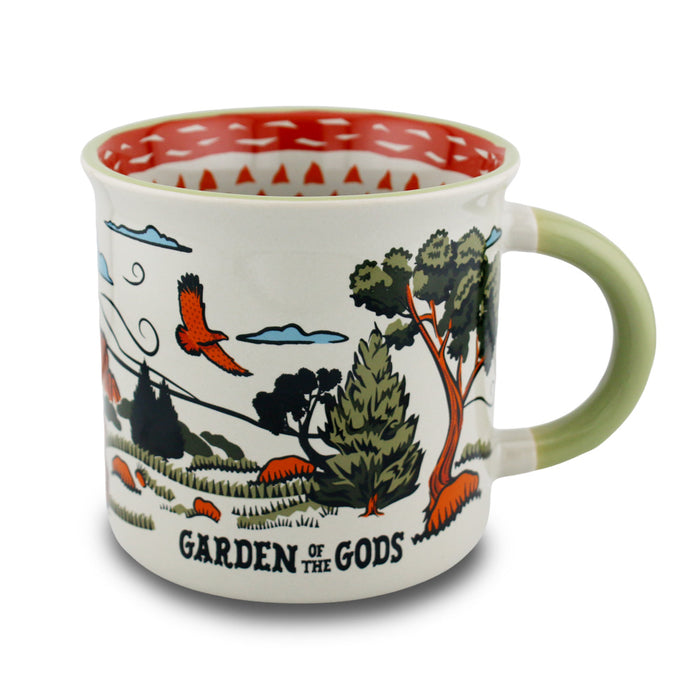 The Garden of the Gods Feeling Folksy Mug is a ceramic mug featuring a green handle and adorned with a scenic nature illustration of red birds, trees, and clouds. “Garden of the Gods” is displayed on the side, celebrating the beauty of Colorado Springs. With its red and white patterned rim and interior, this mug offers a charming tribute to one of Colorado’s most iconic landscapes.