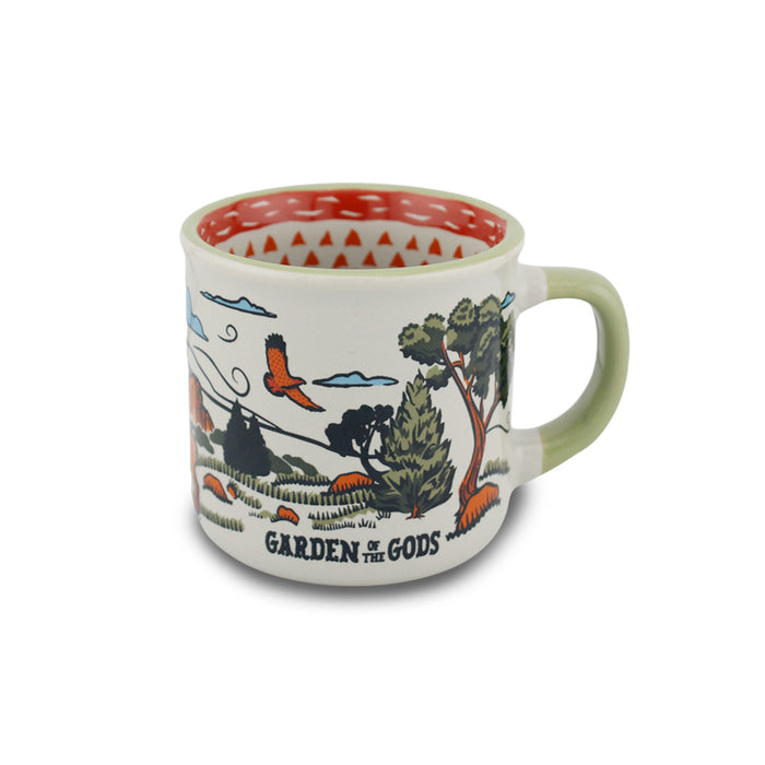 The Garden of the Gods Feeling Folksy Mini Mug makes a perfect Colorado souvenir, featuring an illustrated nature scene with trees, rocks, a bird, and clouds alongside bold Garden of the Gods text. Its white interior is accented with a striking red geometric pattern for added charm.