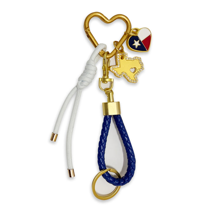 The Texas Carabiner Bag Clip is a gold heart-shaped keychain with three charms: a Texas state outline, a heart with the Texas flag, and a blue braided loop, plus a white cord with gold tips—a stylish accessory for any bag.