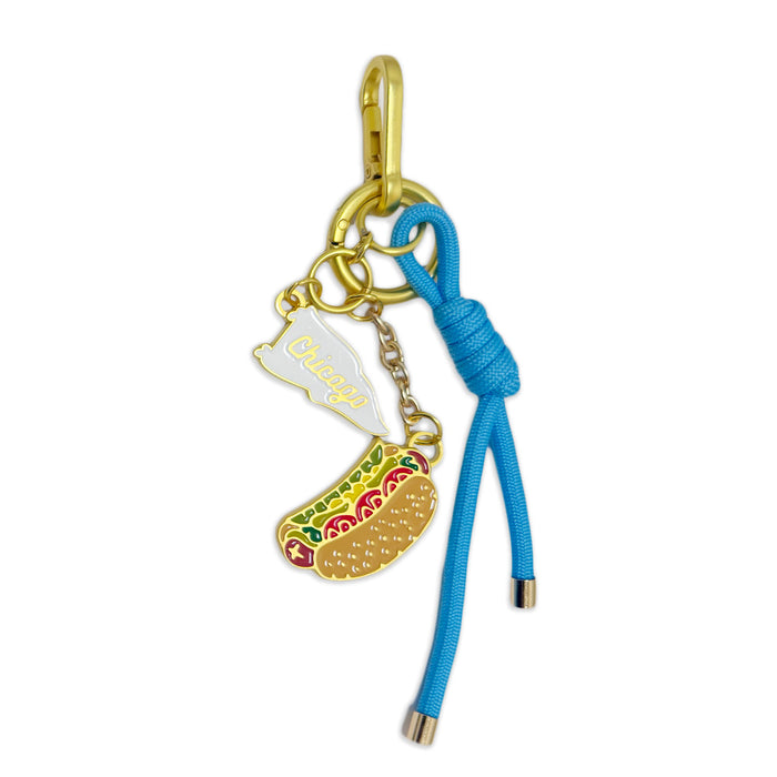The Chicago Icon Dangle Bag Clip features a gold keychain with a blue cord, showcasing two charms: a white Illinois state labeled "Chicago" in gold, and a vibrant hot dog—perfect for celebrating the Windy City's iconic symbols.