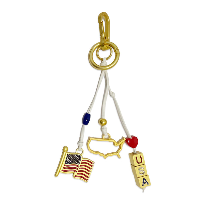 The USA Icon Trio Bag Clip features three charms—a gold USA outline, an American flag, and blocks spelling "USA"—all attached to a gold ring with colored beads and white cords. It's the perfect patriotic accessory for showing your American pride!.
