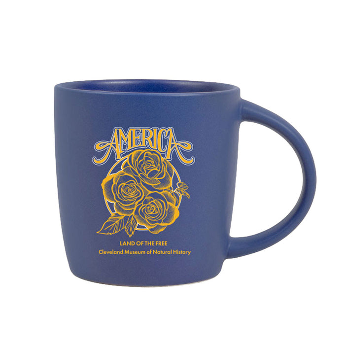The USS Midway Museum America Land of the Free Rose Mug is a blue ceramic mug adorned with a yellow rose design and the phrase “AMERICA LAND OF THE FREE,” evoking patriotic keepsakes from destinations such as the USS Midway Museum or the Cleveland Museum of Natural History.