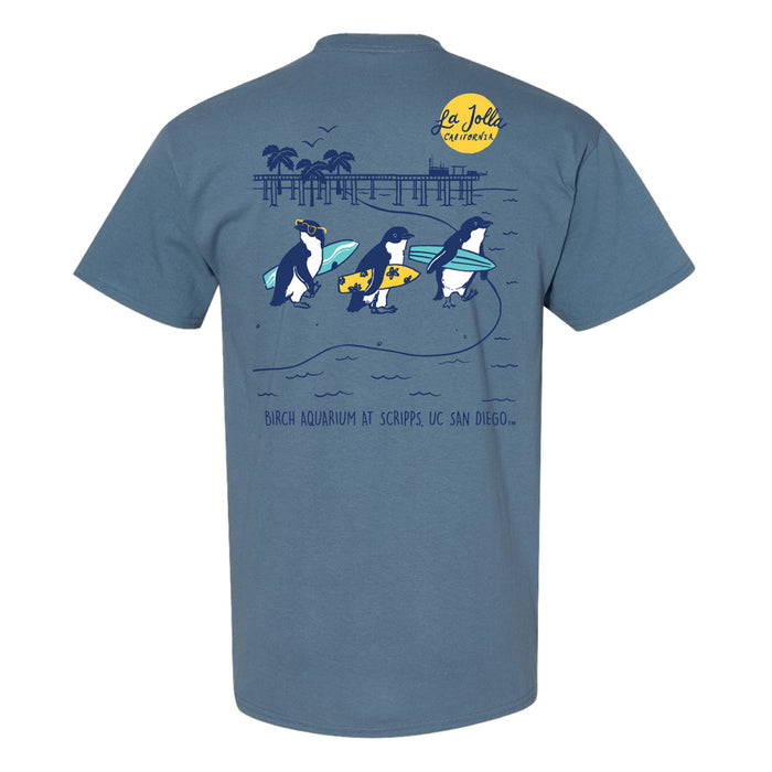Blue t-shirt featuring a graphic of three penguins carrying surfboards near a pier, with the text La Jolla California and Birch Aquarium at Scripps, UC San Diego.
