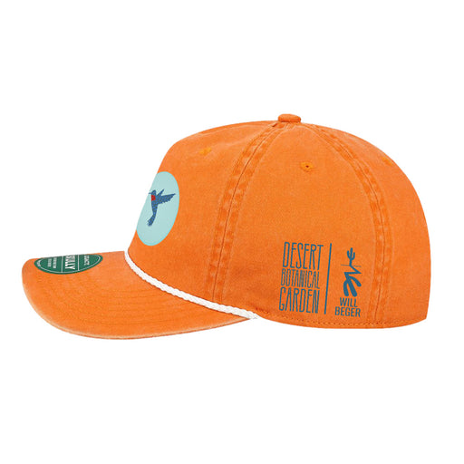The Desert Botanical Garden Will Beger Hummingbird Patch Cap showcases a bright orange design with a vivid blue hummingbird patch on the front, a white-trimmed brim, and “Desert Botanical Garden | Will Beger” alongside a blue cactus logo on the side.