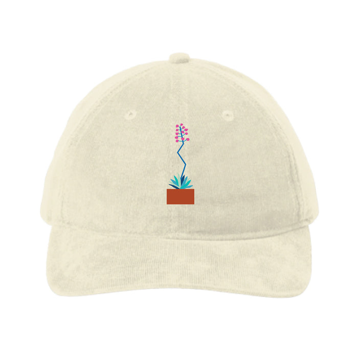 Introducing the Desert Botanical Garden Will Beger Embroidered Agave Flower Cap—a beige baseball cap centered with a small, embroidered potted plant featuring green leaves, a blue stem, and pink flowers. Inspired by Will Beger’s appreciation for the Desert Botanical Garden, this cap adds subtle botanical charm to your everyday style.