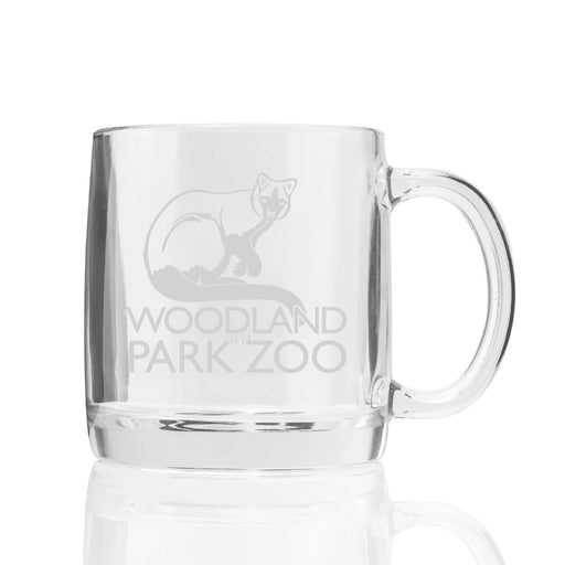 The Woodland Park Zoo Glass Mug features clear glass with an etched small animal above "WOODLAND PARK ZOO." It has a thick handle and is ideal for wildlife conservation fans. Photographed against a white background.