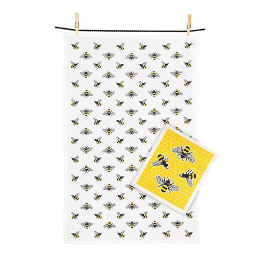 A white eco-friendly kitchen towel with black and yellow bees hangs on a line, next to a yellow card with two bees over honeycomb—both from our Bees Dishcloth & Kitchen Towel Set.