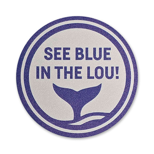 A circular sign with purple text that reads “SEE BLUE IN THE LOU!” above a graphic of a whale tail emerging from water, all on a textured white background.