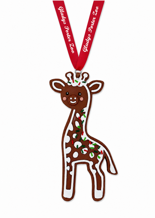 Giraffe-shaped gingerbread cookie ornament with white icing and red and green sprinkles, hanging from a red ribbon labeled Gladys Porter Zoo.