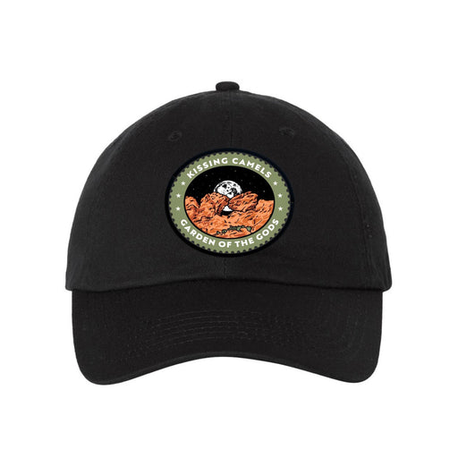 The Garden of the Gods Kissing Camels Cap is a black hat adorned with a patch depicting brown rock formations, a moon, stars, and the words “KISSING CAMELS GARDEN OF THE GODS,” evoking the rugged beauty of Colorado’s Garden of the Gods.