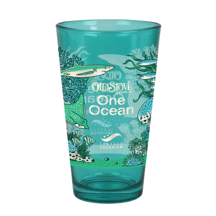 The Seattle Aquarium Old Stove Brewing Co. Pint Glass is a teal glass adorned with ocean animals, plants, and coral. The text on the glass reads “Old Stove Brewing Co., One Ocean, Seattle Aquarium,” with fish and sea life wrapping around the lower half.