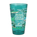 The Seattle Aquarium Old Stove Brewing Co. Pint Glass is a teal glass adorned with ocean animals, plants, and coral. The text on the glass reads “Old Stove Brewing Co., One Ocean, Seattle Aquarium,” with fish and sea life wrapping around the lower half.