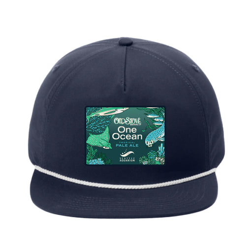The Seattle Aquarium Old Stove Brewing Co. Rope Cap is a navy blue cap with a white rope detail above the brim, showcasing a vibrant patch that reads “One Ocean Pale Ale” alongside ocean-themed illustrations. This cap was created in collaboration with Old Stove Brewing Co., inspired by the spirit of the Seattle Aquarium.