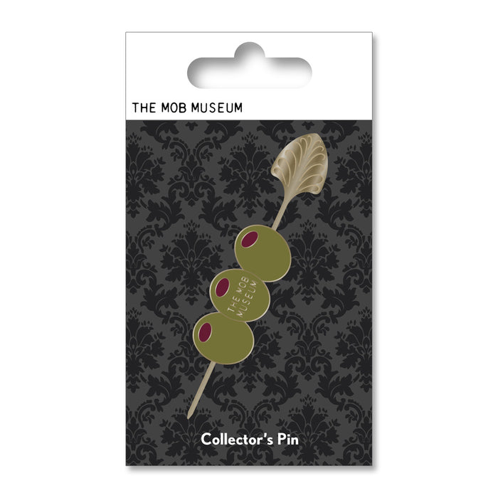 The Mob Museum Cocktail Stirrer Pin showcases three green olives on a cocktail stirrer, with one olive labeled THE MOB MUSEUM, set against a striking black patterned background. Inspired by the Prohibition era, the packaging reads “THE MOB MUSEUM” and “Collectors Pin,” making it an ideal piece for fans of unique memorabilia.