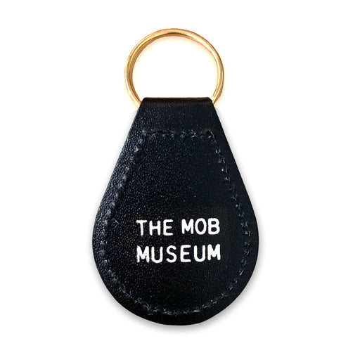 The Mob Museum Teardrop Key Fob is a black leather keychain with a gold keyring, featuring “THE MOB MUSEUM” in bold white capital letters on the front—a sleek souvenir from Las Vegas.