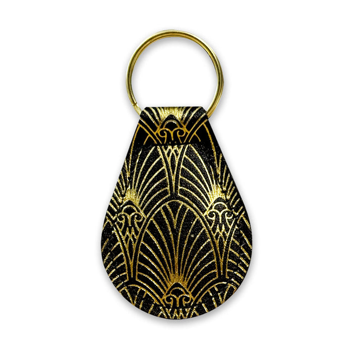 The Mob Museum Teardrop Key Fob features a striking Art Deco pattern in gold set against a black teardrop background, finished with a gold-colored keyring at the top—an elegant accessory that captures the glamorous spirit of Las Vegas and serves as an ideal keepsake for fans of the Mob Museum.