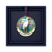 The Naples Botanical Garden Egret Ornament showcases a white heron standing amid purple flowers beneath a vibrant sky, with “Naples Botanical Garden” inscribed below—an ideal Florida keepsake presented in a dark blue box.