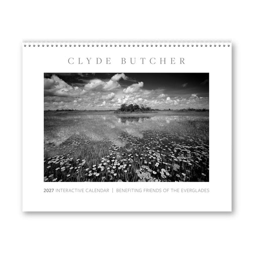 The Clyde Butcher 2027 Interactive Calendar features a striking black-and-white cover image of a wetland landscape with wildflowers, reflective water, and clouds. Showcasing captivating landscape photography by Clyde Butcher, this calendar supports Friends of the Everglades.