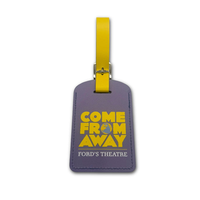 The Ford’s Theatre Come From Away Luggage Tag is a purple accessory featuring the Tony Award-winning musical’s title and Ford’s Theatre in bold yellow and white text, attached to a yellow strap, and is displayed against a white background.