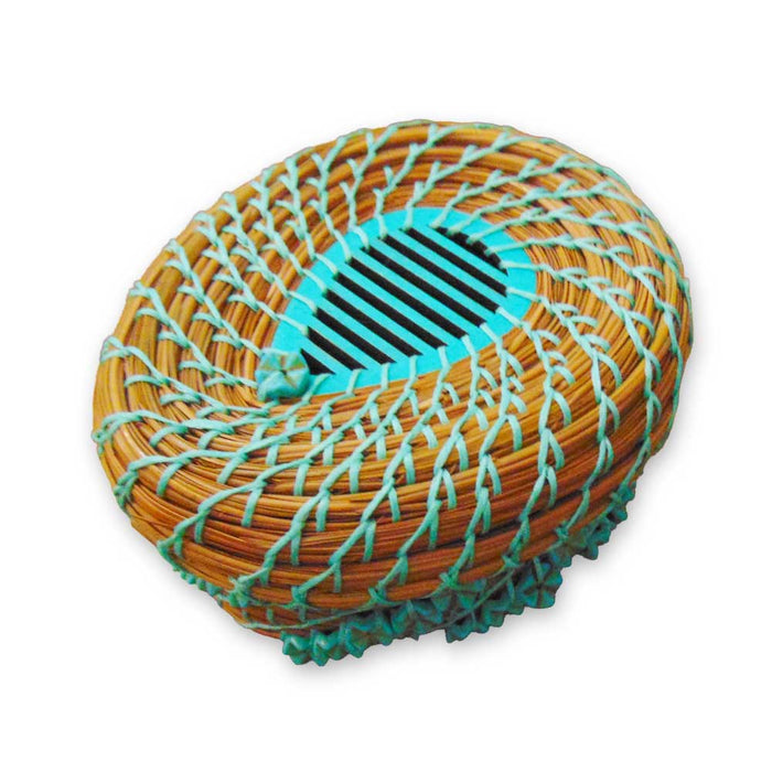 Introducing the Turquoise Pine Needle Basket: a round, handwoven wicker basket adorned with a striking spiral pattern and covered by a decorative net of light blue string. This eco-friendly piece features a slotted blue-green circular opening at the center, making it an ideal choice for those seeking unique, sustainable decor.