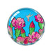 Desert Botanical Garden Superbloom Paper Weight featuring a circular glass design with a hummingbird hovering over blooming pink cactus flowers against a bright blue background.