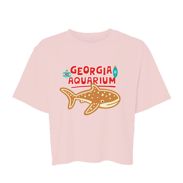 Georgia Aquarium Holiday Whale Shark Crop T-Shirt in light pink, featuring a gingerbread-style whale shark, two Christmas ornaments, and the text Georgia Aquarium.