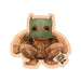 A Thomas Dambo, Trolls Field Study Magnet featuring a wooden sculpture of a crouching troll wearing a green box over its head, with the text Trolls Field Study printed in the corner.