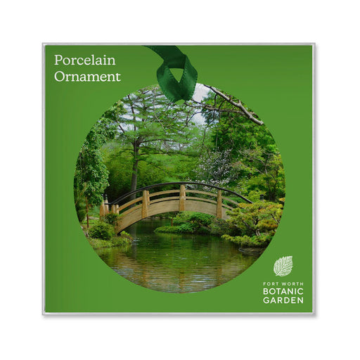 Square packaging for a Fort Worth Botanical Garden Ornament, featuring a circular image of a wooden arched bridge over a pond in the garden.