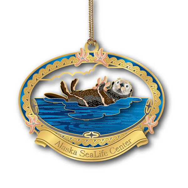 The Seattle Aquarium Sea Otter Ornament features a sea otter floating on its back among starfish in an ornate gold and blue frame—perfect for holiday décor with a “Seattle Aquarium” banner at the bottom.