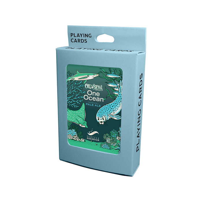 A blue box of Seattle Aquarium Old Stove Brewing Co. Playing Cards, created in partnership with Old Stove Brewing Co. and the Seattle Aquarium, displays illustrated sea animals such as a shark and seal on the front. The box features a hanging tab and the words “PLAYING CARDS” repeated along the sides and top.