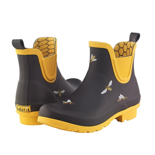 The Black Bees Chelsea Rainboot is a comfy short black rain boot with yellow soles and trim, bee and honeycomb patterns, pull tabs, and a Galleria label—ideal for stylish wet-weather outings.
