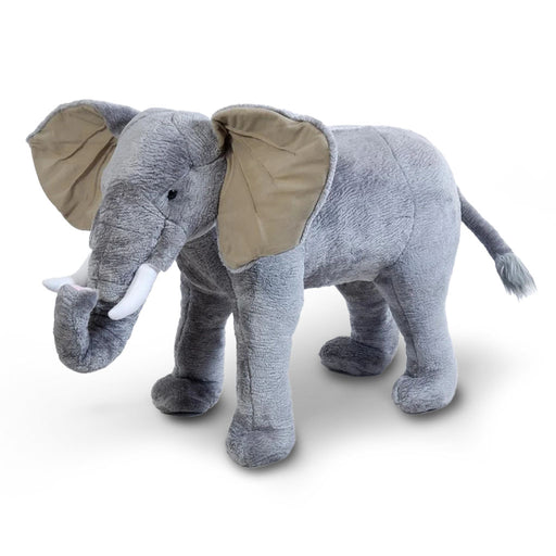 The Ride-on Extra Large Elephant Plush is a big gray toy with floppy ears, white tusks, and a raised trunk, standing on all fours—ideal for imaginative play.