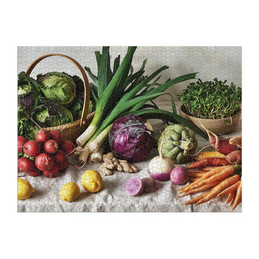 The Greenmarket Table 1500 Piece Puzzle showcases a vibrant still life of fresh vegetables—a basket of leafy greens, leeks, red cabbage, radishes, lemons, ginger, turnips, and carrots—for a colorful puzzle challenge.