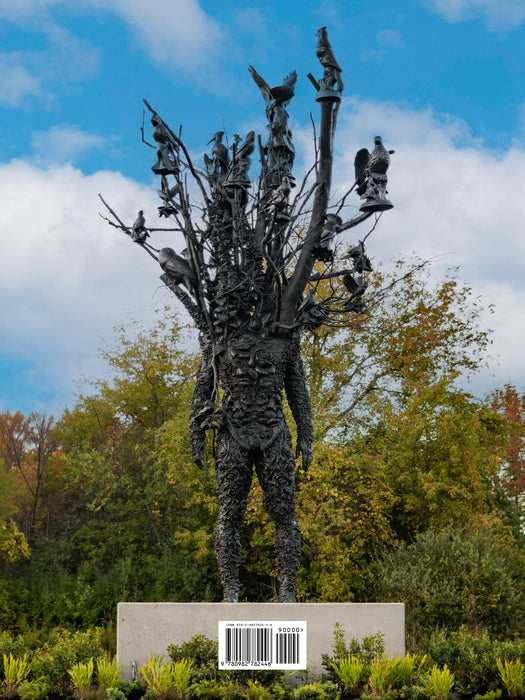 A sculpture of a human figure with branches and birds extending from its upper body stands on a pedestal outdoors at Frederik Meijer Gardens, enveloped by lush greenery. A barcode is visible on the base. The partly cloudy sky enhances the tranquil atmosphere—an ideal scene highlighted in the Guide to Collections & Gardens for anyone exploring the sculpture park.