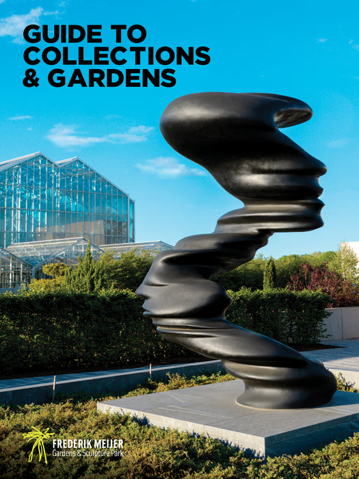 A twisting black sculpture of abstract human faces stands in front of a modern glass conservatory at Frederik Meijer Gardens & Sculpture Park under a blue sky, greeting visitors with a striking introduction to the renowned sculpture park—just one of many highlights featured in the Guide to Collections & Gardens.