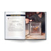 An open copy of Chicago Cocktails: An Elegant Collection of Over 100 Recipes Inspired by the Windy City (City Cocktails) displays a Third Coast Cocktail recipe on the left, while on the right, a person positions a drink beneath a glass smoking box. A patterned glass and an indistinct figure appear in the background—offering an enticing look at inventive Chicago cocktails and the artistry found within this sophisticated collection.