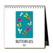 A spiral-bound Butterflies 2027 Desk Calendar featuring a teal rectangle with a circle of colorful butterflies, labeled at the bottom.