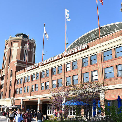 The exterior of the Chicago Childrens Museum, a red-brick building with flags above and people walking outside on a sunny day.