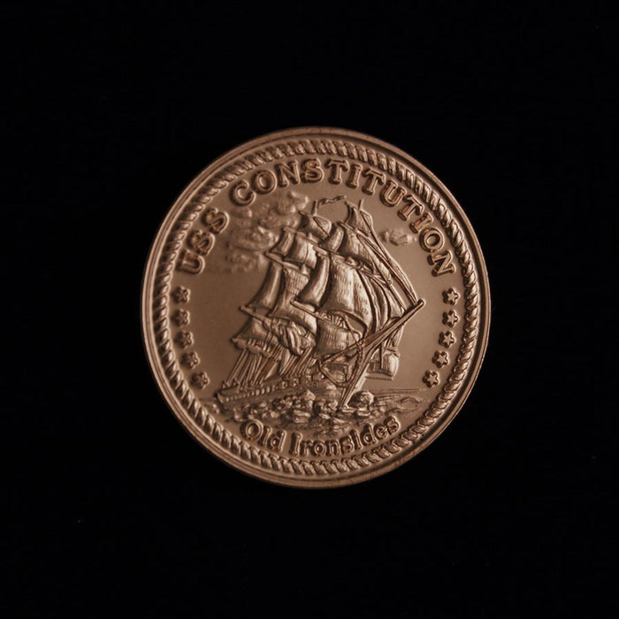 The USS Constitution Limited Edition Collector's Medallion is a bronze coin with a detailed sailing ship engraving, "USS CONSTITUTION" at the top, "Old Ironsides" below, all set against a bold black background.